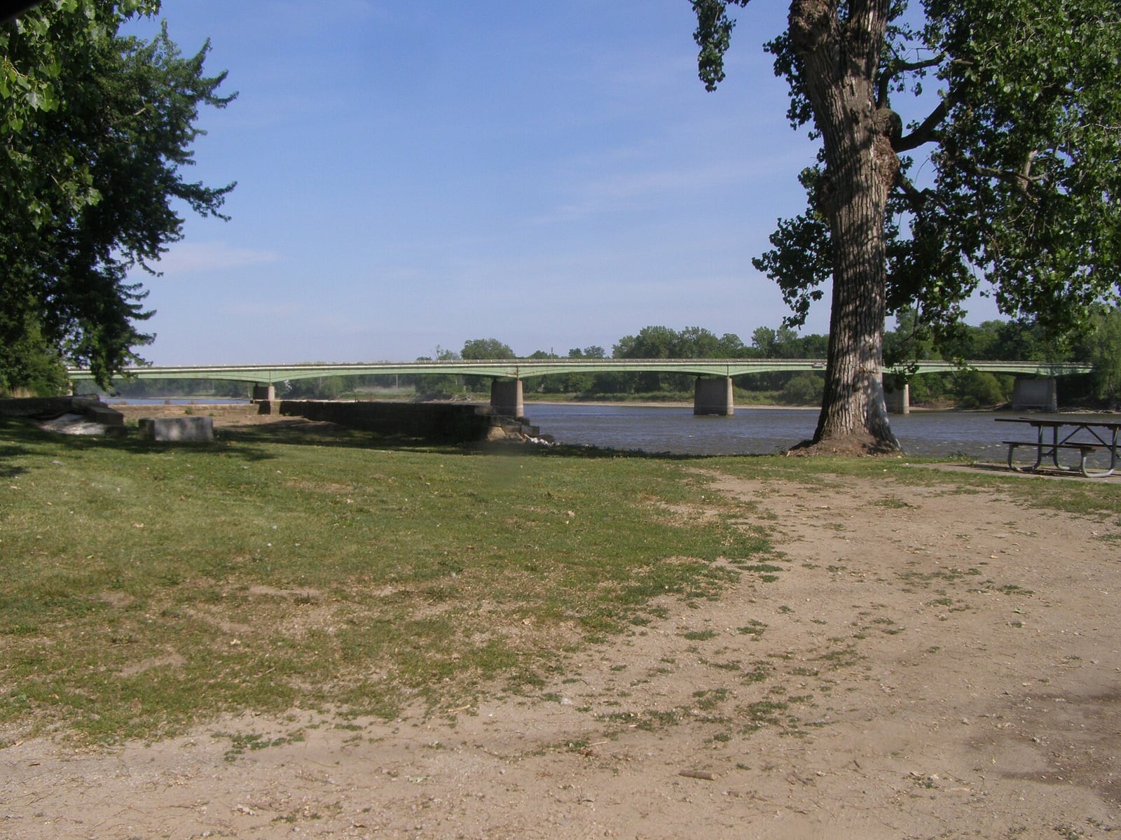 The Des Moines River flows past Bonaparte riverfront buildings and the old lock structure under a bright sky.