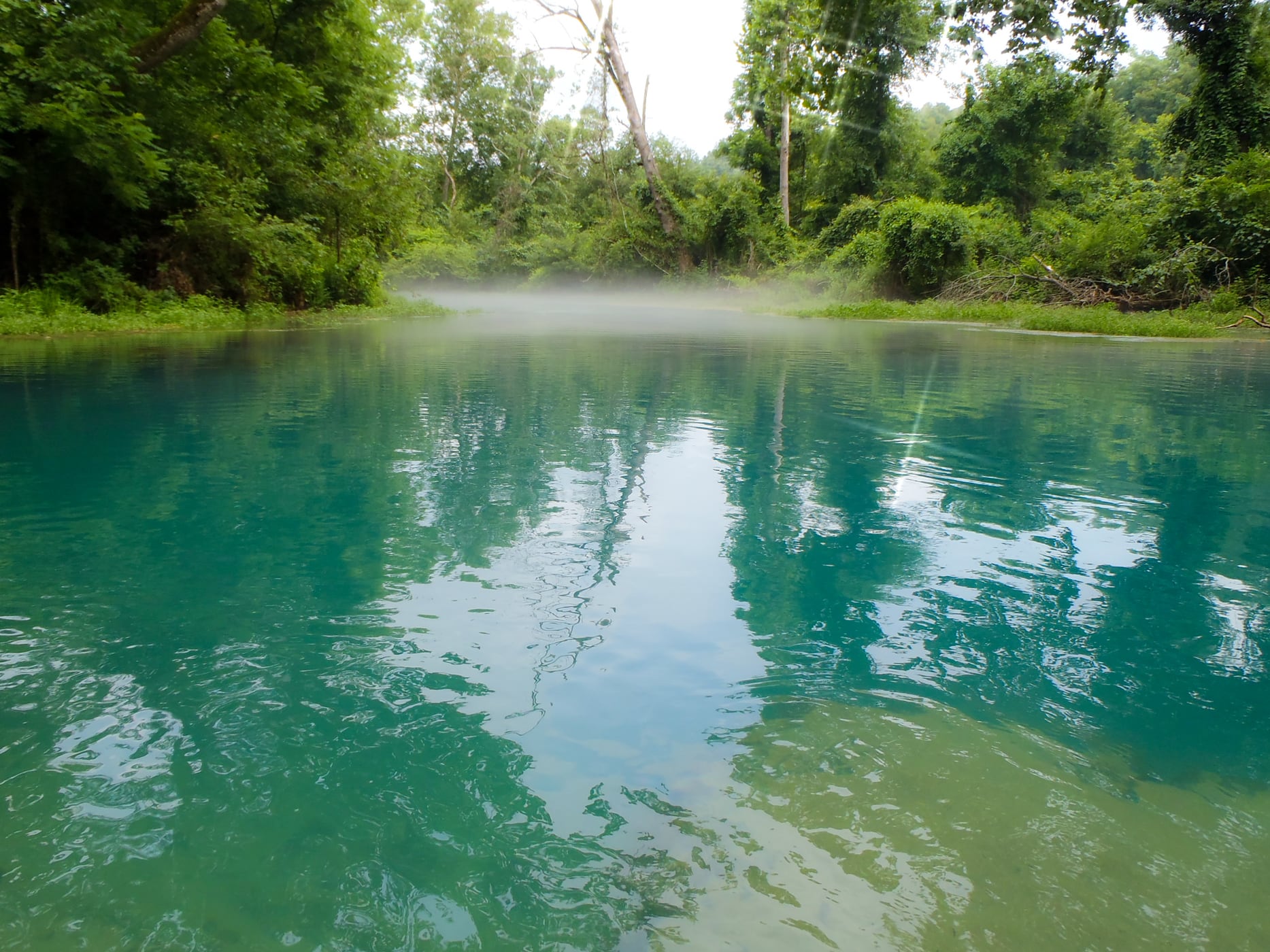A canoe rests beside the clear Eleven Point River with wooded Ozark banks rising behind the channel.