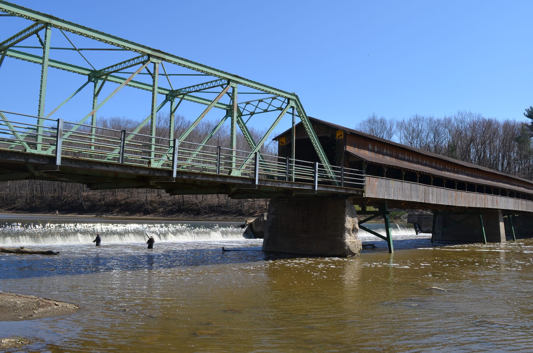 The Harpersfield covered bridge and adjacent road bridge cross the Grand River above low ledges and brown spring water.