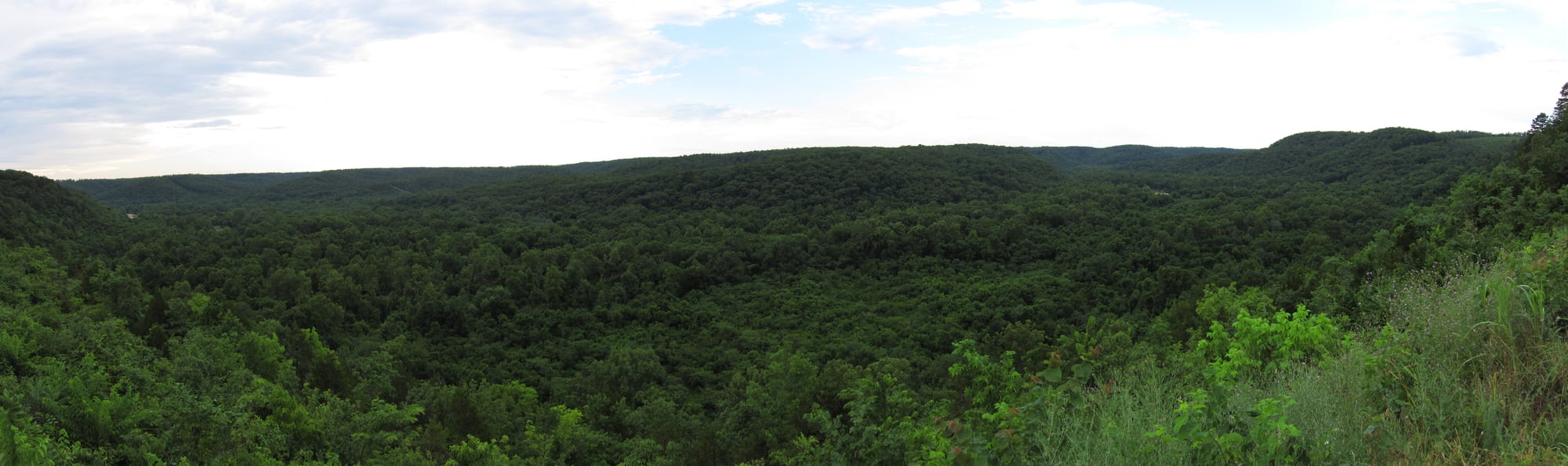 The upper Jacks Fork River winds below wooded Ozark hills with a gravel bar along the clear channel.