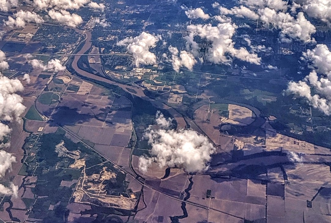 An aerial view shows the Kansas River with broad sandbars, wooded banks, and bridges in the distance.