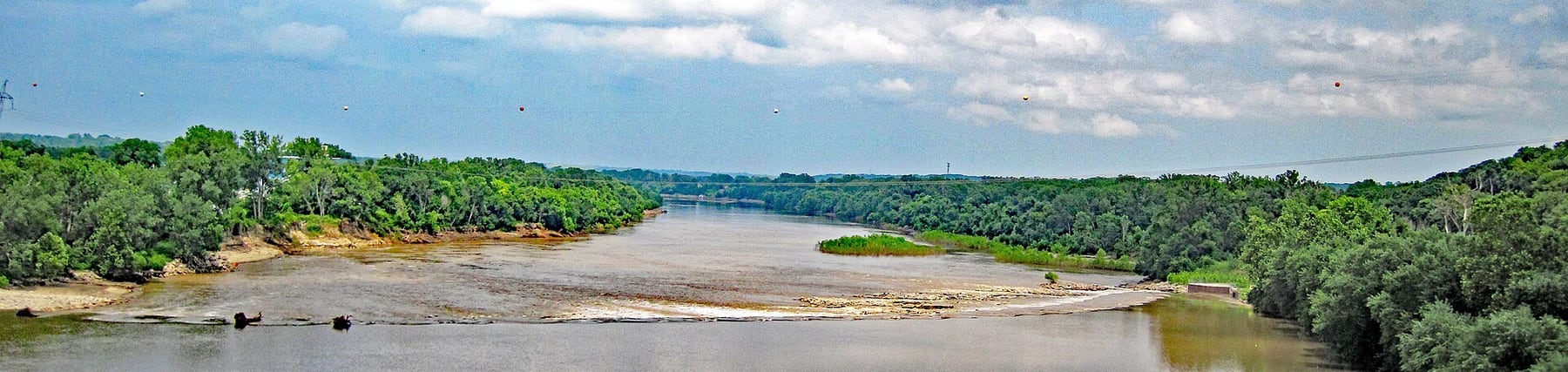The Kansas River flows through Kansas City with exposed sand and a low bridge crossing the wide channel.