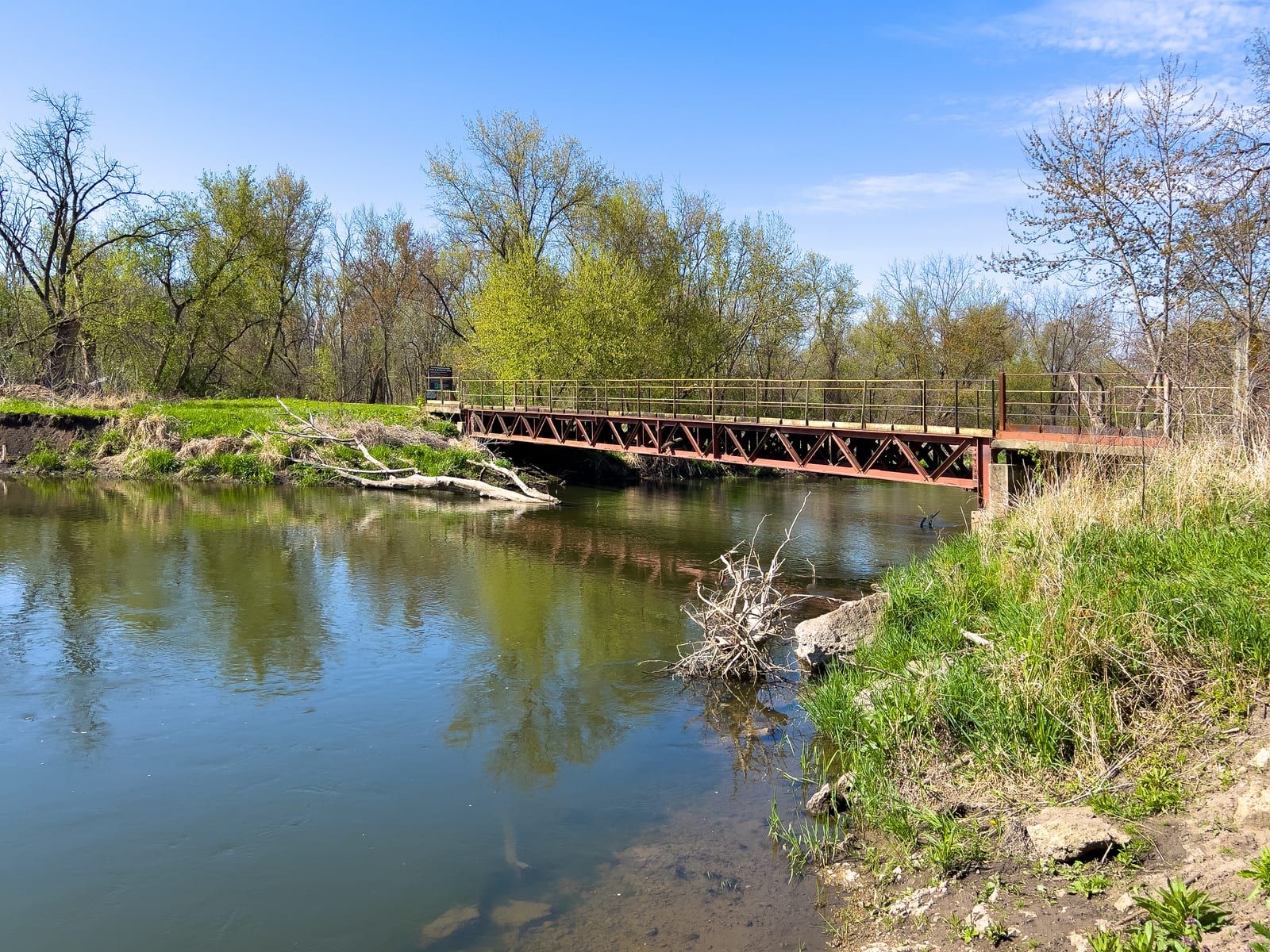 A low bridge crosses the Kishwaukee River in a wooded state fish and wildlife area corridor.