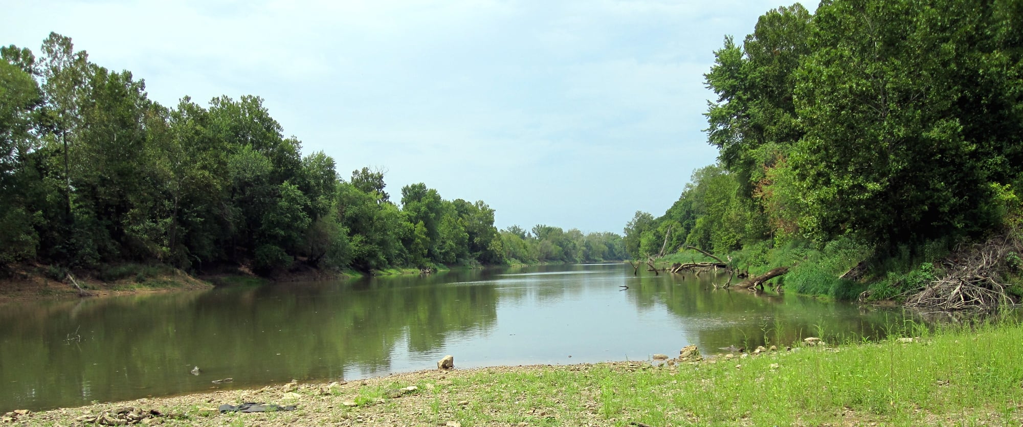 The Meramec River bends below a wooded bank in Missouri under a broad summer sky.