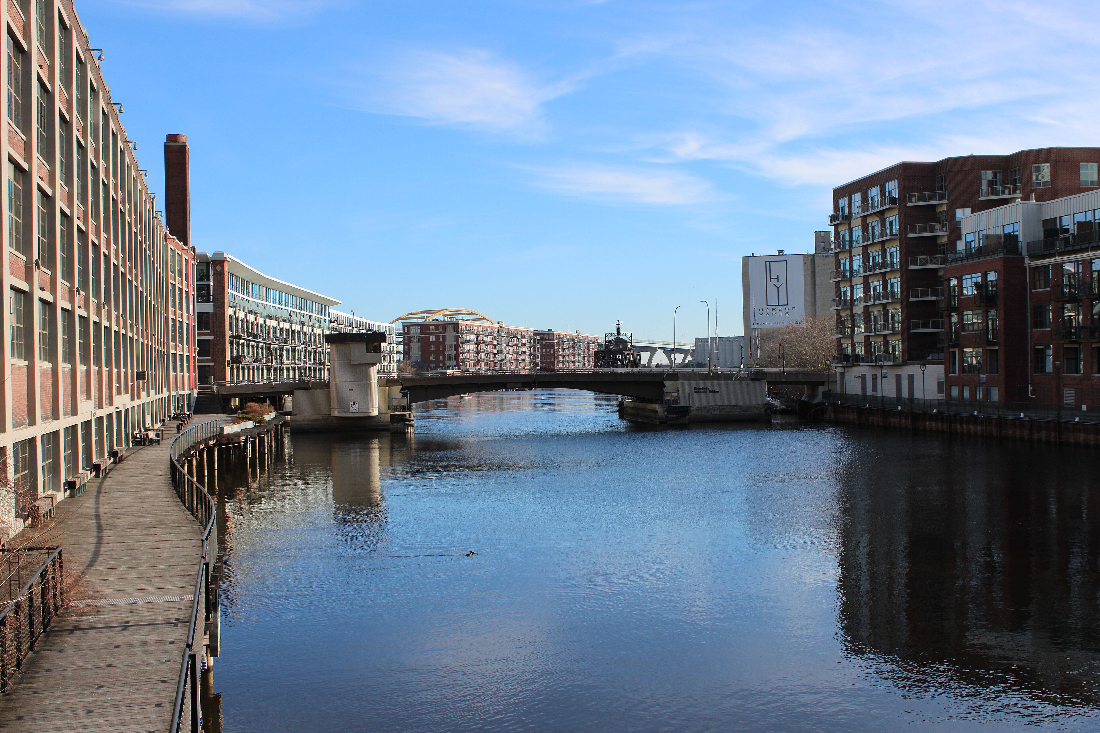 The Milwaukee River flows through an urban winter corridor with snowy banks and bare trees.