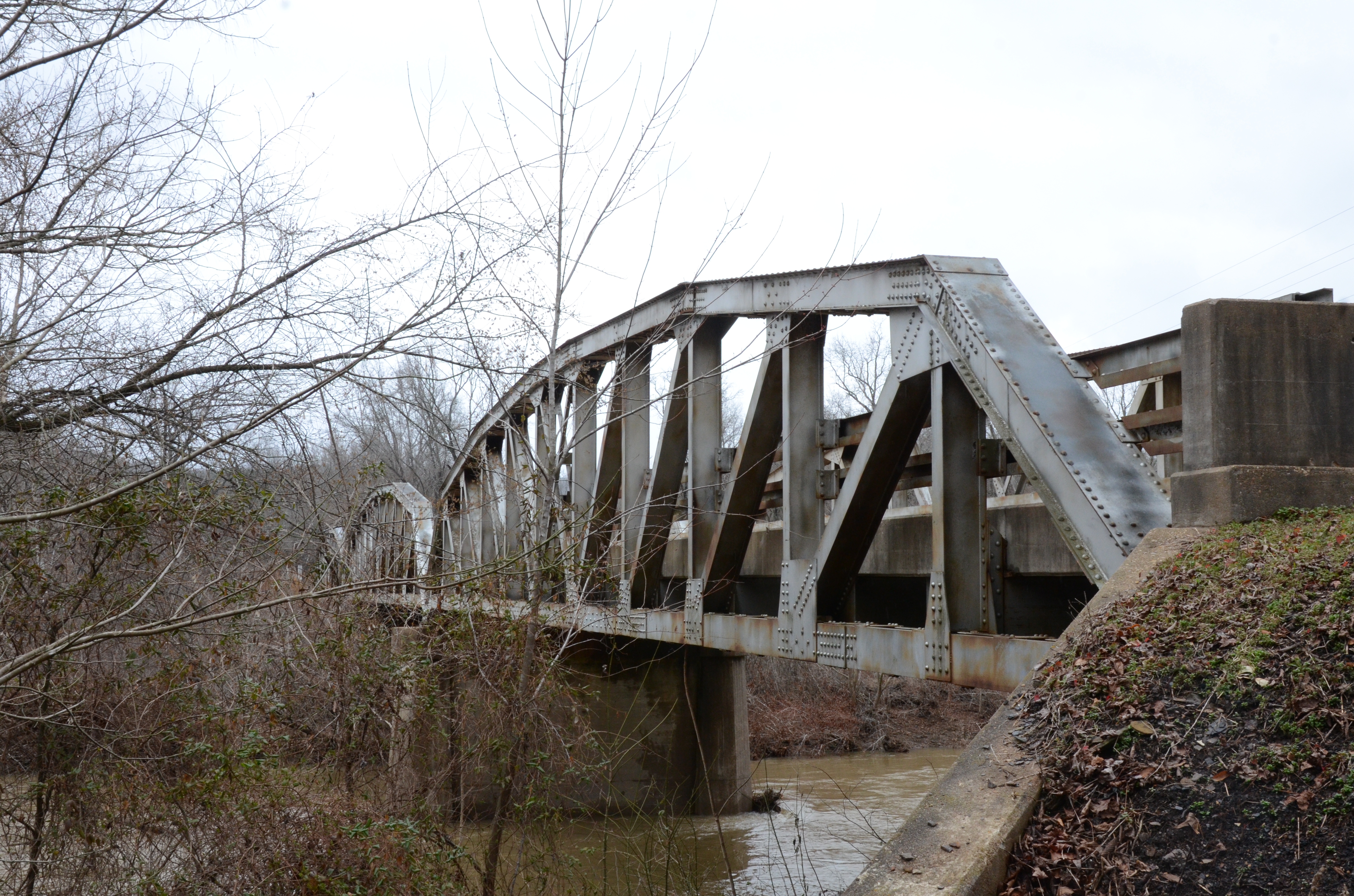 A steel truss bridge crosses the Mulberry River above a rocky channel lined with spring-green trees.