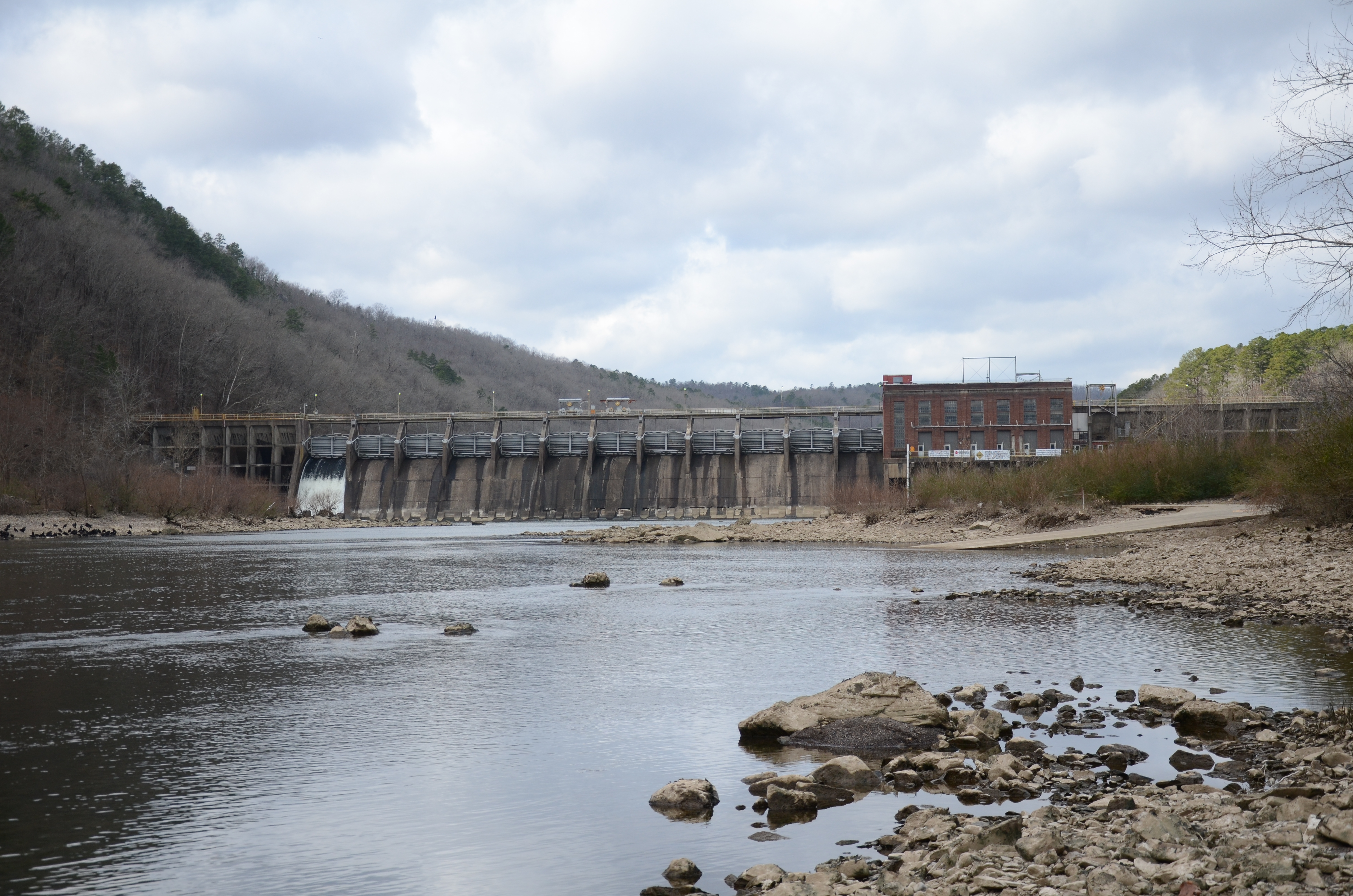 Remmel Dam spans the Ouachita River with release water below the concrete spillway and wooded banks nearby.